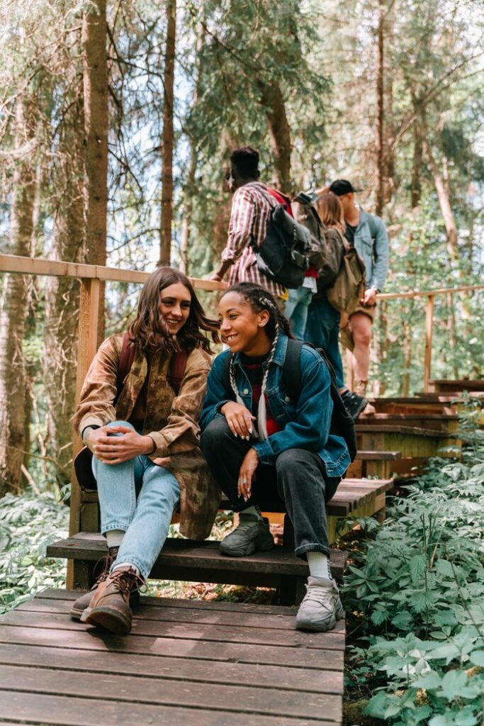 A group of friends sitting and chatting on wooden stairs in a lush forest setting.